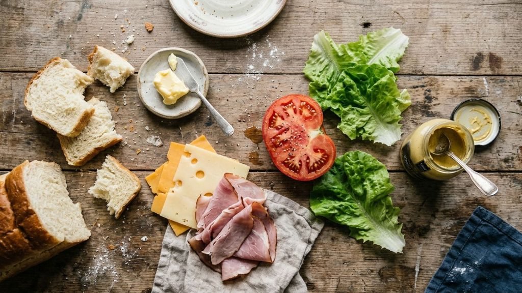 Flat lay of sando sandwich ingredients including milk bread, cheese, ham, tomato, and mustard
